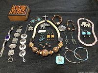 Photo showing entire lot with wooden jewelry box and various fashion jewelry pieces including bracelets, necklaces, earrings, and pendants arranged on black surface.