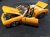 Model Camaro with open hood, doors, and seats visible on black background showing yellow-orange body and detailed engine.