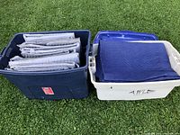 Two plastic bins filled with various folded moving blankets, mostly grey and blue in color.