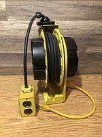 Yellow Safeway retractable electric cord reel with black accents and attached 4-plug outlet box. Power cord wound around reel.