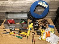 Overview of the lot showing the metal tool box and multiple hand and electrical tools arranged on a wood surface
