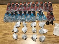 Wide view showing multiple packs of screws in clear packaging labeled with size SM-02 and others, along with several small wrapped packages and two black cabinet knobs on wood surface.