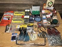 Full lot overview of assorted hardware items including packs of screws, washers, hose clamps, a padlock, and insulation kit on a wooden table.