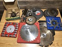 Photo showing large assortment of different saw blades, grinding discs, wire brushes, and a rotary garden weeder tool in a box.