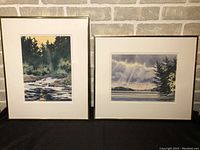 Both watercolor paintings in gold-tone frames, showing river scene and lake scene.