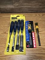 Photo showing the full set of 6 wood carving chisels including Stanley three-piece set, two additional wood handle chisels, and Fuller Pro chisel in original packaging.