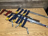 Overall view of the wood clamps laid out on a table showing six clamps including blue and yellow bar clamps and red F-clamps.