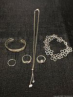 View of all silver jewelry items on black fabric including bracelets, rings, and necklace