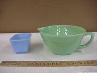 Photo showing side view of the green Fireking bowl with handle and pouring spout alongside the smaller blue square Pyrex bowl with ruler for scale.