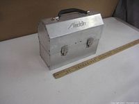 Full view of the vintage aluminum lunch pail with brand embossed on the front and a ruler for size reference.