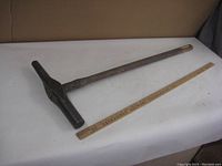 Full view of the antique spike sledge hammer laid next to a wooden ruler for scale showing the overall length and condition.