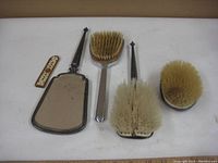 Photo showing antique grooming items including the fold-away comb, hand mirror, and three brushes from top view