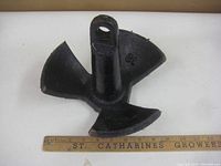 Top view of black plastic-coated boat anchor showing three flukes and attachment eyelet with ruler for scale.