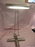 Desk lamp showing full height and heavy weighted metal base with horizontal tubular shape and dual rods supporting cylindrical shade.