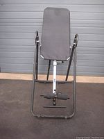Front view of inversion table with padded backrest and ankle supports against a garage door background.