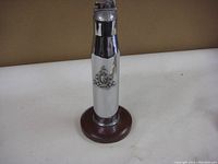 Full view of chrome plated bullet shell lighter with Canadian Corps of Signals badge mounted on a wooden base.