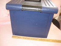 Blue plastic file box with black handle and ruler for size reference placed in front of it.