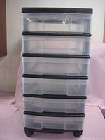 Full front view of the plastic storage unit showing six transparent drawers in a black frame on caster wheels.
