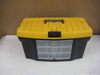 Front view of the black and yellow plastic tool box on a white surface against a beige background