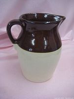 Front and side views of the two-tone pottery jug showing shape, handle, and spout, along with a ruler indicating approximate height of 9.5 inches.