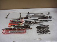 Tools laid out on white surface including coping saw, cement drill bits in and out of packaging, ratchet handles, socket extensions, and adaptors.