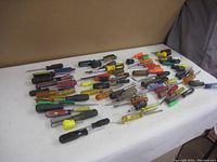 Wide shot of approximately 40 screwdrivers and nut drivers spread on a white surface highlighting handle variety and tool lengths.