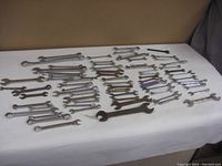 Wide view of a large collection of combination and open-end wrenches in imperial and metric sizes spread out on a white surface.