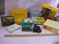 Vintage camera and movie accessory lot showing boxes, film reels, and devices for splicing and changing film.