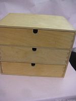 Front view of rectangular wooden box with three drawers and half-circle cutout handles.