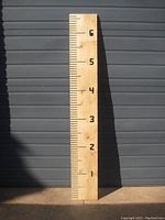 Full view of the wooden growth chart board standing vertically against a dark wall, showing the numbered measurement markings from 1 to 6 feet and detailed routered numbering.