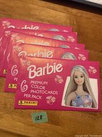 Five unopened sealed pink packs of 1999 Barbie Premium Color Photocards from Panini on a wooden surface.