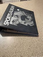 Black Sports Album binder with 'Sports Album' printed on the cover holding hockey cards.