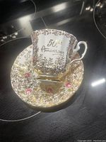Side view of the Elizabethan Fine Bone China teacup resting on matching saucer, showing gold floral pattern and 50th Anniversary text.