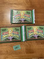 Photo of three unopened 1994 Mighty Morphin Power Rangers premium trading card packs with green packaging and logo, laid out on a wooden surface.