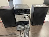 Front view of Sony HCD-FX300i stereo system with two black Sony speakers, remote control, and dock station visible.