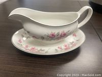 Side view of vintage white ironstone gravy boat with pink rose decorations on matching underplate.