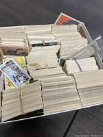 High angle view of a box filled with hundreds of vintage trading cards stacked and rubber-banded mostly on their edges, showing some fronts and backs with various illustrations.