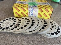 Stack of multiple View-Master reels showing circular white cardboard discs with black image windows, some printed text visible