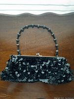 Black hand purse with shiny black sequins and beaded handle on a wooden surface