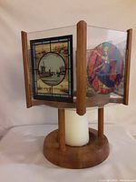 Front view of candle holder with two stained glass panels visible showing ship and royal guard artwork. Wooden frame and base with white pillar candle inside.