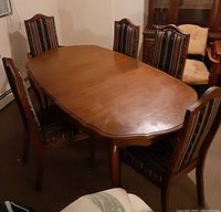 Photo of the oval wood dining table with five matching fabric-upholstered chairs around it, showing the table surface and chair design.