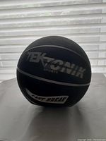 Black Tektonik basketball with grey branding placed on a white surface in front of a window with blind.