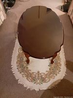 Top-down view of the dark brown polished cherry wood oval coffee table on a floral rug, showing shape and finish.
