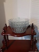 Five crystal serving bowls stacked on a small wooden stand, showing diamond-patterned texture and clear glass material.