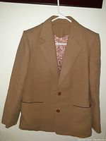 Front view of custom made brown women's blazer hanging on white plastic hanger showing two front buttons and front pockets.