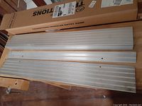 Three aluminum modular ramp sections placed on wooden floor, showing ridged anti-slip surfaces with pre-drilled holes for assembly.