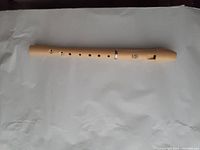 Plastic soprano recorder flute lying flat on white paper background, showing mouthpiece and finger holes.