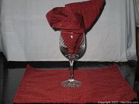 Red cloth napkin folded and placed inside a wine glass with one napkin laid flat under the glass.