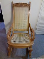 Front view of the wooden rocking chair showing the carved backrest and wicker seat and backrest.