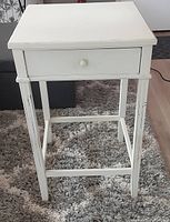 Front view of the white side table showing drawer and leg structure with some scratches.